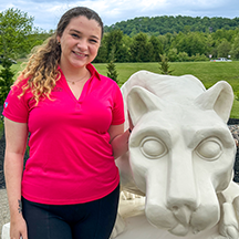 PSU-LV female student in bright pink New Student Orientation leader shirt smiling, standing next to the PSU-LV lion shrine.