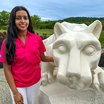 PSU-LV female student in bright pink New Student Orientation leader shirt smiling, standing next to the PSU-LV lion shrine.