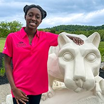 PSU-LV female student in bright pink New Student Orientation leader shirt smiling, standing next to the PSU-LV lion shrine.