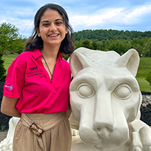 PSU-LV female student in bright pink New Student Orientation leader shirt smiling, standing next to the PSU-LV lion shrine.