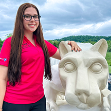 PSU-LV female student in bright pink New Student Orientation leader shirt smiling, standing next to the PSU-LV lion shrine.