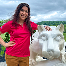 PSU-LV female student in bright pink New Student Orientation leader shirt smiling, standing next to the PSU-LV lion shrine.