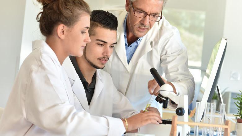 Three people in lab coats at microscope