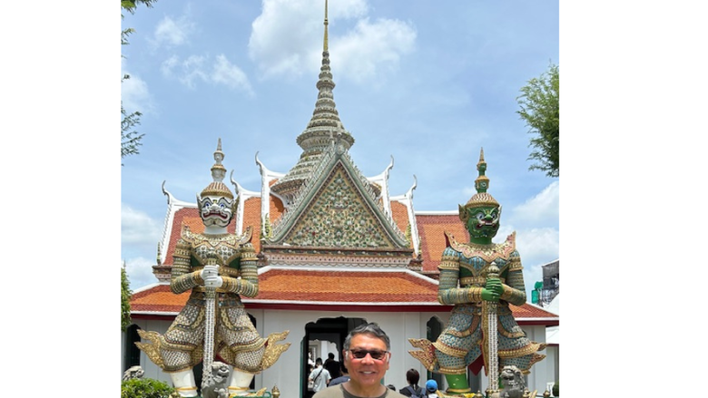 a man smiles in front of an ancient temple in Thailand